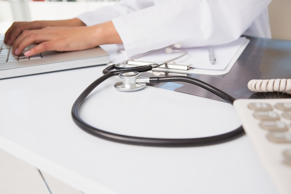 Doctor using laptop near stethoscope and clipboard in medical office